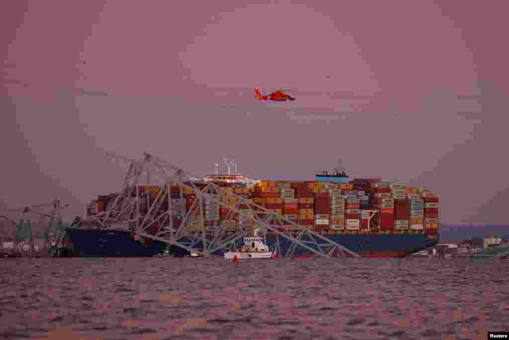 A helicopter flies over the scene of the Francis Scott Key Bridge collapse in Baltimore, March 26, 2024. 