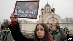 Seorang perempuan memegang potret Alexey Navalny dan istrinya, Yulia, di luar gereja tempat pemakamannya berlangsung, di Moskow, Rusia, 1 Maret 024. (Foto: AP Photo)