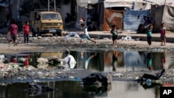 FILE - Displaced children walk through a dark streak of sewage flowing into the streets of Deir al-Balah, central Gaza Strip, Aug. 29, 2024.