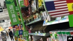 FILE - Women push a shopping cart near items imported from the United States at a supermarket in Beijing, April 2, 2018. 