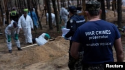 FILE - A war crimes prosecutor stands as experts work at a forest grave site during an exhumationin the town of Izium in Kharkiv region, Sept. 18, 2022. 