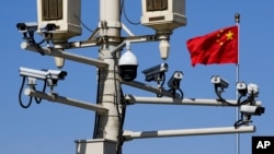 FILE - A Chinese national flag flutters near surveillance cameras mounted on a lamp post in Tiananmen Square in Beijing, China, March 15, 2019. 
