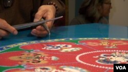 Mandala artist Losang Samten is dispensing sand using metal tools called Chakpur, which he has been using for more than 30 years to create mandalas. (VOA/ J. Soh)