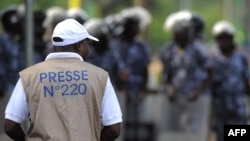Un journaliste examine les forces de sécurité debout pour empêcher une foule de plusieurs centaines de journalistes et de membres du public de manifester devant le Palais des Congrès de Lomé, le 19 février 2013.