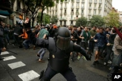A Spanish riot policeman swings a club against would-be voters near a school assigned to be a polling station by the Catalan government in Barcelona, Oct. 1, 2017.