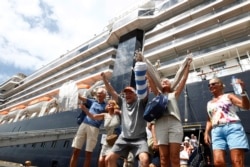 FILE - Passengers react after they disembark from the MS Westerdam, back, at the port of Sihanoukville, Cambodia, Friday, Feb. 14, 2020. Hundreds of cruise ship passengers long stranded at sea by virus fears cheered as they finally disembarked Friday.