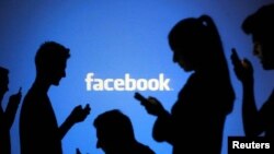People are silhouetted as they pose with laptops in front of a screen projected with a Facebook logo, file photo.