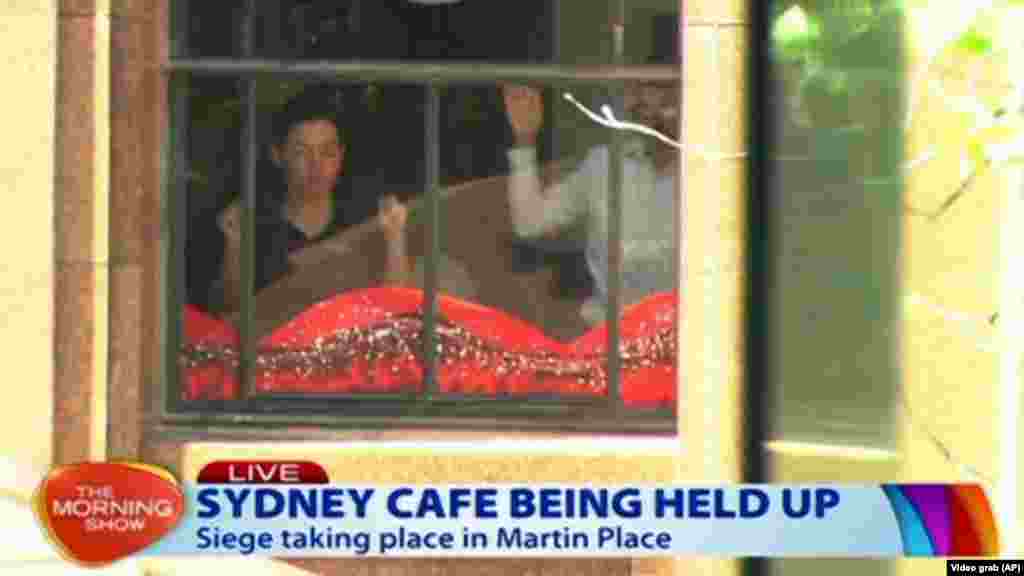 This image taken from video shows people holding up hands inside a cafe in Sydney, Australia, Dec. 15, 2014. 