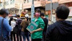 FILE - A staffer holds the government's QR code for the LeaveHomeSafe COVID-19 mobile app as people line up to get the COVID-19 coronavirus vaccine in Hong Kong, Nov. 29, 2021.