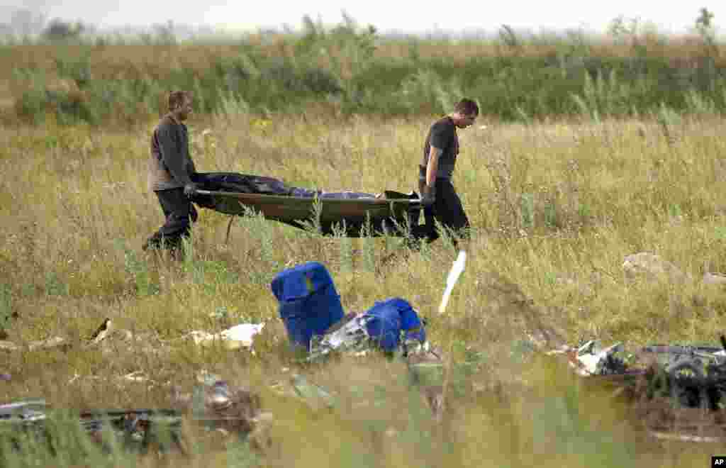 Para petugas darurat membawa jenazah di lokasi jatuhnya pesawat Malaysia Airlines penerbangan MH17 dekat desa Hrabove, Ukraina timur (19/7). (AP/Vadim Ghirda)