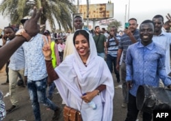 FILE - Alaa Salah flashes the victory gesture and shouts slogans while marching during a demonstration in front of the military headquarters in the capital Khartoum, April 10, 2019.