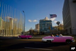 FILE - Tourists ride in classic American convertible cars past the United States embassy, right, in Havana, Cuba, Jan. 12, 2017.