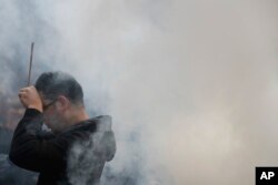 A Chinese man is covered by incense smoke as he offers prayers on the first day of the new year at Beijing's Yonghegong Lama Temple as the Chinese capital is blanketed by heavy smog, Jan. 1, 2017.