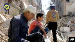 In this picture provided by the Syrian Civil Defense group known as the White Helmets, residents sit amongst rubble in rebel-held eastern Aleppo, Syria, Oct. 11, 2016. Damascus and Moscow insist they are not targeting the city's civilians, as ample evidence seems to point to the contrary.
