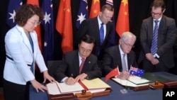 Australian Prime Minister Tony Abbott, back center, watches as China's Minister of Commerce Gao Hucheng, second left, and Australian Minister for Trade Andrew Robb, second right, sign a free trade agreement between the two countries in Canberra, Australia