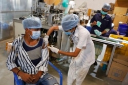 An Indian health worker administers the Covishield vaccine for COVID-19 to a worker at the factory of a face mask manufacturer on the outskirts of Ahmedabad, India, Dec. 17, 2021.