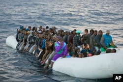 FILE- In this Feb. 3, 2017 file photo, migrants and refugees wait to be helped by members of the Spanish NGO Proactiva Open Arms, as they crowd aboard a rubber boat sailing out of control in the Mediterranean Sea about 21 miles north of Sabratha, Libya.