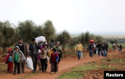 Internally displaced people walk with their belongings in the town of Inab, eastern Afrin, Syria, March 14, 2018.