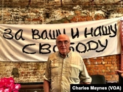 Pavel Litvinov at a Moscow exhibit to mark the 50th anniversary of his demonstration against the Soviet Union's invasion of Czechoslovakia in 1968. Behind him is a reproduction of the banner he and 7 other protesters unfurled on Red Square. It reads: "For Your Freedom and Ours."