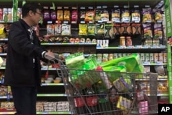 FILE - A man pushes a shopping cart past a display of nuts imported from the United States and other countries at a supermarket in Beijing, Apr. 2, 2018.