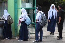 Seorang satpam memeriksa suhu tubuh seorang siswa sebelum memasuki sekolahnya pada hari pertama pembukaan kembali sekolah menengah negeri di Bekasi, 13 Juli 2020. (Foto: AP/Achmad Ibrahim)