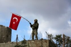 Seorang tentara Turki mengibarkan bendera di Gunung Barsaya, timur laut Afrin, Suriah, 28 Januari 2018. (Foto: REUTERS/Khalil Ashawi)