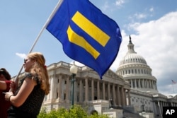 FILE - A supporter of LGBT rights holds up an "equality flag" on Capitol Hill in Washington, July 26, 2017.
