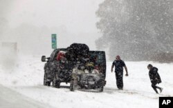 People attend to their vehicle on Interstate 26, near Savannah, Ga., Jan. 3, 2018. A brutal winter storm dumped snow in Tallahassee, Fla., Wednesday for the first time in nearly three decades before slogging up the Atlantic coast.