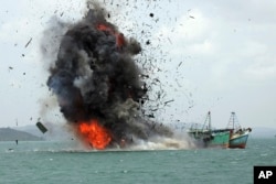 FILE - Debris flies into the air as illegal fishing boats are blown up, Feb. 22, 2016, by the Indonesian Navy off Batam Island, Indonesia. Blowing up illegal vessels has become somewhat of a local tourist attraction in Indonesia.