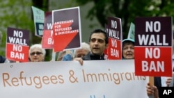 FILE - Protesters hold signs during a demonstration against President Donald Trump's revised travel ban, May 15, 2017, outside a federal courthouse in Seattle.