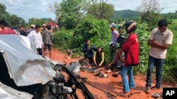 In this photo provided by Cambodia National Police, onlookers stand around the mangled wreckage of Cambodia's Prince Norodom Ranariddh's car after a collision with another vehicle outside Sihanoukville, Cambodia, Sunday, June 17, 2018.