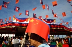 FILE- A Cambodian woman holds a Chinese flag as she walks a friendship bridge between Cambodia and China during its inauguration ceremony in Takhmao, Kandal provincial town, south of Phnom Penh, Cambodia.