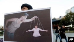 Seorang mahasiswi Korea Selatan memegang poster yang menggambarkan Presiden Korea Selatan Park Geun-hye (kanan bawah) sebagai boneka dan Choi Soon-sil, orang kepercayaannya, sebagai dalang, di Seoul (3/11).