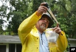 Robert Muxo of the Miami-Dade County Mosquito Control department, takes a sample of water that was standing in a potted plant in Miami, June 21, 2016. The department was responding to complaints about mosquitoes by a neighborhood resident.