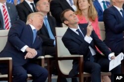 FILE - French President Emmanuel Macron, right, and U.S. President Donald Trump watch the traditional Bastille Day military parade, including military jet flyovers, on the Champs Elysees, in Paris, July 14, 2017.