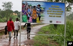 FILE - People walk past a billboard warning residents to stop the stigmatization of Ebola survivors, in Kenema, eastern Sierra Leone, Aug. 12, 2015.