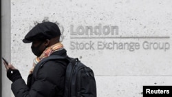 A man wearing a face mask walks past a bank electronic board showing the Hong Kong share index at Hong Kong Stock Exchange, June 9, 2020. 