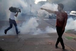 FILE - A protester argues with law enforcement officers as a reporter runs from tear gas during a demonstration against the death in Minneapolis police custody of George Floyd, in Saint Paul, Minnesota, May 31, 2020.