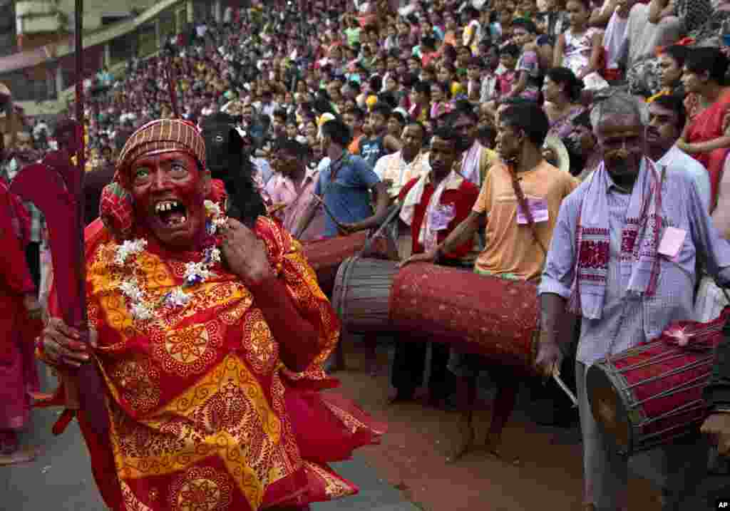 A Hindu priest, face smeared with color and sacrificial blood, carries a goat over his shoulder for sacrifice during the Deodhani festival at the Kamakhya Hindu temple in Gauhati, India