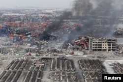 Smoke rises among shipping containers next to damaged vehicles as firefighters try to put out a fire after explosions on Wednesday night, at Binhai new district in Tianjin, China, Aug. 14, 2015.