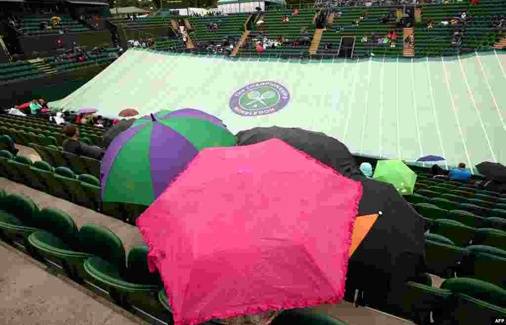 Penonton duduk di bawah payung di lapangan dua ketika hujan mulai turun pada hari kelima Kejuaraan Wimbledon 2014 di The All England Tenis Club di Wimbledon, London barat daya.