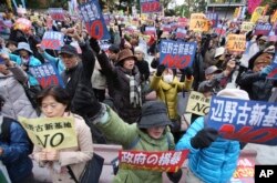 FILE - Anti-U.S. base protesters hold placards with a slogan that reads: "No to Henoko new base" during a rally in Tokyo.