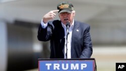 Republican presidential candidate Donald Trump gestures to a his camouflaged "Make America Great" hat as he discuses his support by the National Rifle Association at a campaign rally at the Redding Municipal Airport, June 3, 2016, in Redding, California.