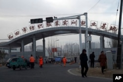 In this Wednesday, Dec. 5, 2018, photo, residents pass by the entrance to the "Hotan City apparel employment training base" where Hetian Taida has a factory in Hotan in western China's Xinjiang region. (AP Photo/Ng Han Guan)