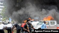 FILE - People extinguish vehicle fires caused by a bomb explosion near the parliament building in Kampala, Uganda, on Nov. 16, 2021.