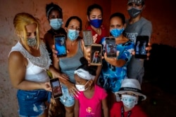 Zuleydis "Zuly" Elledias, left, shows a cellphone photo of her missing husband to a child while her neighbors pose for a group picture holding up cellphone photos of their missing relatives who ventured out in homemade boats in an attempt to reach Florida