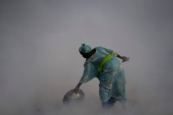 Ndeye Yacine Dieng drops embers over peanut shells covering fish as she walks amidst the smoke on Bargny beach, some 35 kilometers (22 miles) east of Dakar, Senegal, Wednesday April 21, 2021.