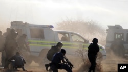 Polisi di tengah-tengah gas air mata dan debu mengarahkan tembakan ke arah para pekerja di pertambangan Lonmin di Rustenburg (16/8). 