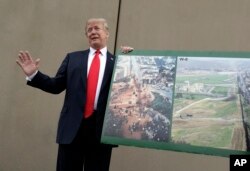 FILE - President Donald Trump holds a photo of the border area as he reviews border wall prototypes, March 13, 2018, in San Diego.