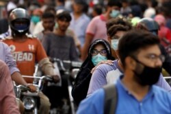 seorang wanita mengendarai sepeda motor saat dia mengenakan masker pelindung di tengah serbuan orang di luar pasar ketika wabah penyakit coronavirus (COVID-19) berlanjut, di Karachi, Pakistan 8 Juni 2020